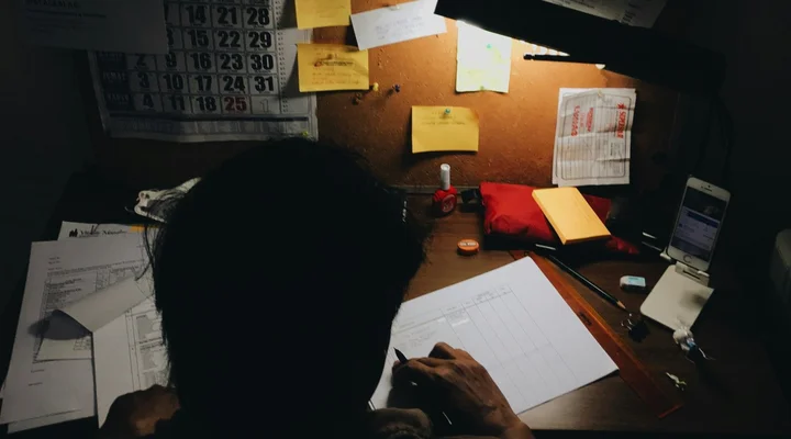 Artisan remplissant ses devis le soir sous une lampe de bureau, entouré de factures et post-its